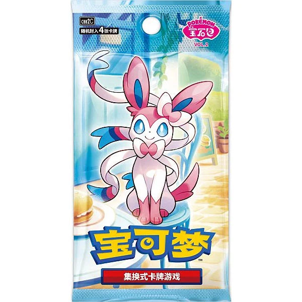 The Pokémon TCG: Gem Pack Vol. 2 Booster Pack (Kinesisk) by The Pokémon Company features Sylveon on the packaging, highlighted with Chinese text and vibrant blue, pink, and yellow colors. Showcasing a bright indoor scene with a table and window in the background, this booster pack is perfect for collectors of kinesiske Pokémon kort and fans of Eevee’s evolutions.