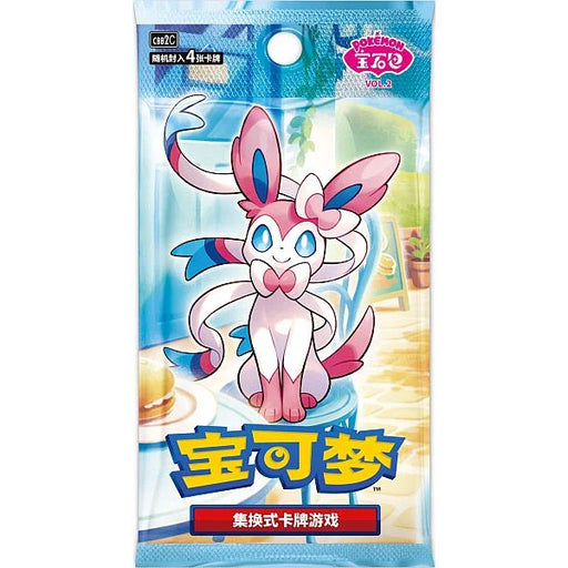 The Pokémon TCG: Gem Pack Vol. 2 Booster Pack (Kinesisk) by The Pokémon Company features Sylveon on the packaging, highlighted with Chinese text and vibrant blue, pink, and yellow colors. Showcasing a bright indoor scene with a table and window in the background, this booster pack is perfect for collectors of kinesiske Pokémon kort and fans of Eevee’s evolutions.